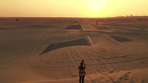 Vue de dos femme blonde cheveux avec sac à dos authentique jaune regardant sur la route sablonneuse après tempête de sable. Aventures de voyage dans le désert.