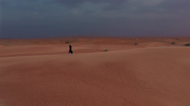 Luftaufnahme von einer Drohne, die neben einer Frau in Abaya fliegt, vereinigte arabische Emirate in traditioneller Kleidung auf den Dünen in der Wüste — Stockvideo