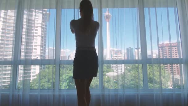 Женщина открывает занавес на больших окнах с видом на город с зеленым гадерном и зданиями. Концепция зеленого города. — стоковое видео