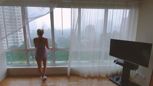 Rückansicht einer Frau, die durch das Fenster auf die Stadt im Regen blickt. — Stockvideo