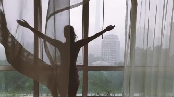 Zadní pohled na ženu dívající se oknem na město v dešti. — Stock video