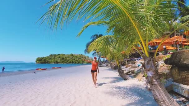 SLOW MOTION. Young woman weared in orange t-shirt walking on the beach — Stock Video