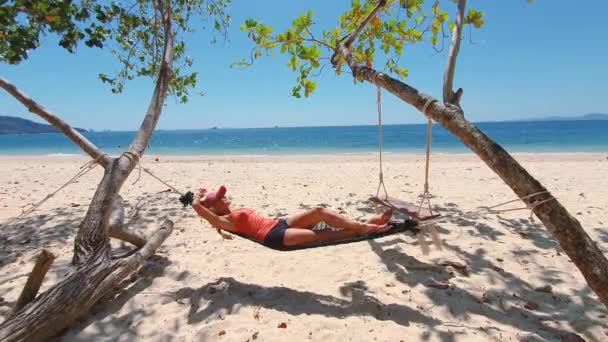 Woman in orange t-shirt and hat on the beach in hammock. — Stock Video