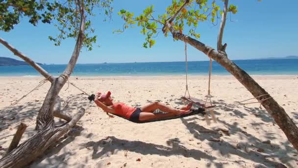 Mujer en camiseta naranja y sombrero en la playa en hamaca. — Vídeos de Stock