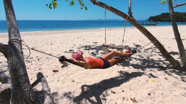 Kvinna i orange t-shirt och hatt på stranden i hängmatta. — Stockvideo