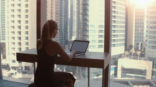 Mujer en cuarentena con portátil trabajando cerca de la ventana con vista a la ciudad . — Vídeos de Stock