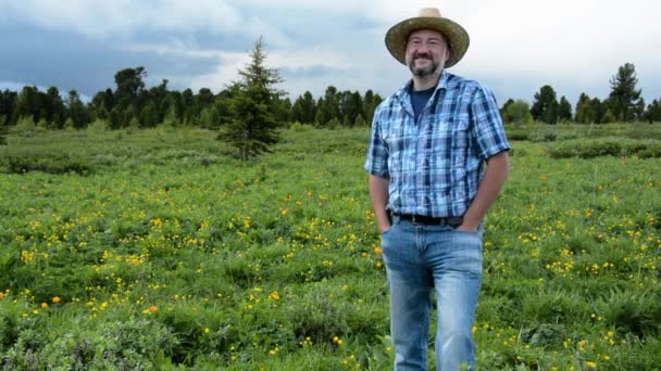 花のある高い山の畑を背景に藁帽子をかぶった男農家 — ストック動画