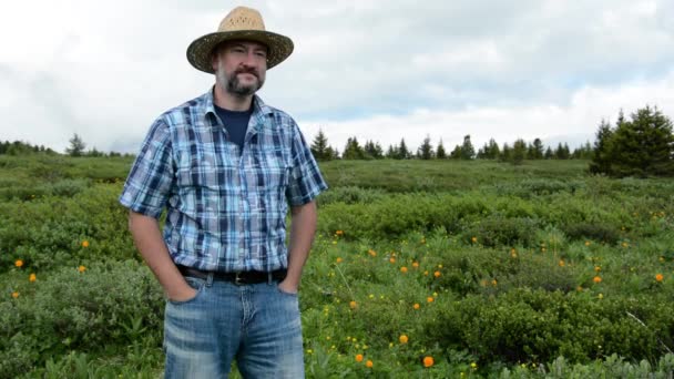 Hombre agricultor en un sombrero de paja sobre un fondo de un campo de alta montaña con flores — Vídeo de stock