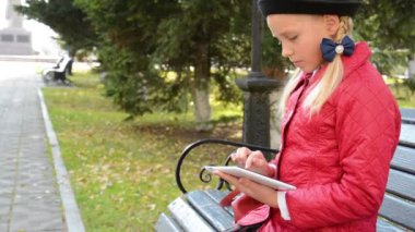 Tablet bilgisayar ile genç kız şehir parkında sonbaharda bankta oturur. Onun tablet bilgisayarda oyun oynayan kız