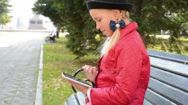 Tablet bilgisayar ile genç kız şehir parkında sonbaharda bankta oturur. Onun tablet bilgisayarda oyun oynayan kız
