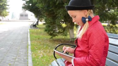Tablet bilgisayar ile genç kız şehir parkında sonbaharda bankta oturur. Onun tablet bilgisayarda oyun oynayan kız