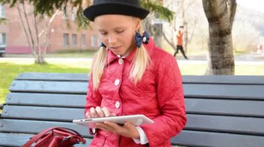 Tablet bilgisayar ile genç kız şehir parkında sonbaharda bankta oturur. Onun tablet bilgisayarda oyun oynayan kız