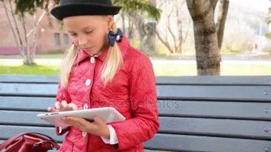 Tablet bilgisayar ile genç kız şehir parkında sonbaharda bankta oturur. Onun tablet bilgisayarda oyun oynayan kız