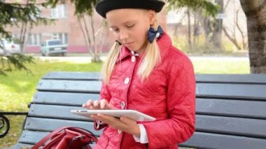 Tablet bilgisayar ile genç kız şehir parkında sonbaharda bankta oturur. Onun tablet bilgisayarda oyun oynayan kız