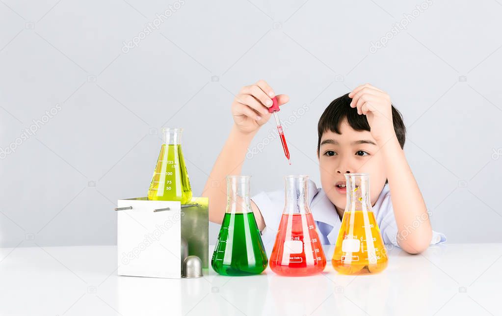 Little scientist boy with colorful beaker on white table