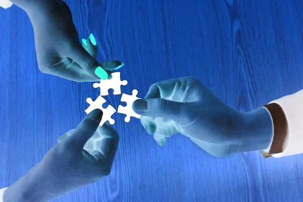 Close up abstract image of three hands business people holding jigsaw puzzle on wooden table with negative light, Concept teamwork and brainstorm