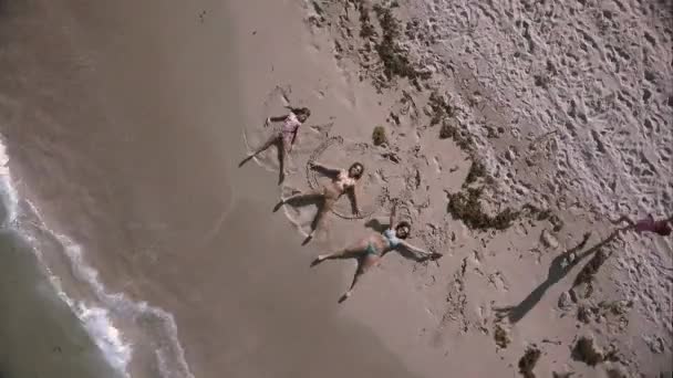 Super vzdušný spřádání střílel na pláži se třema holkama dělá Pískoví andílci a jeden dělá hvězdu vedle oceánu.