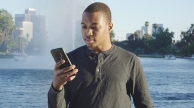 Genç Afrikalı Amerikalı adam telefonuna bakıyor, şaşırmış ve mutlu davranıyor.