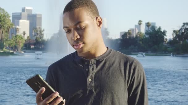 Young african american man using his cellphone in front of lake — ストック動画