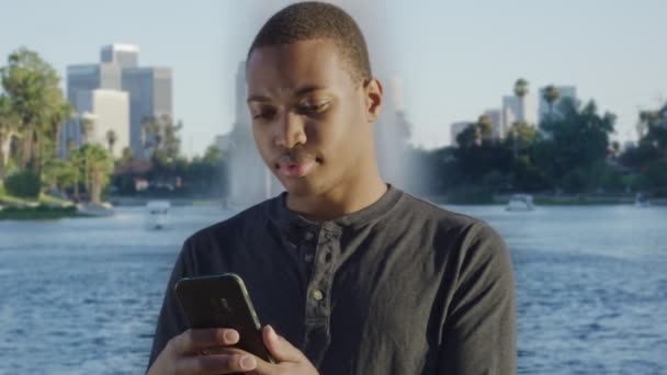 Jonge Afro-Amerikaanse man met behulp van zijn mobiele telefoon in de voorkant van het meer — Stockvideo
