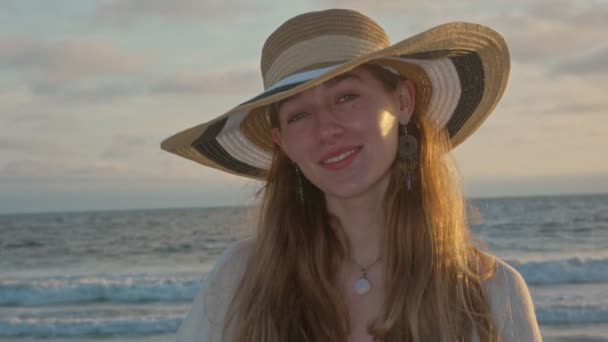 Belle jeune femme au bord de l'océan souriant à la caméra pendant le coucher du soleil — Video