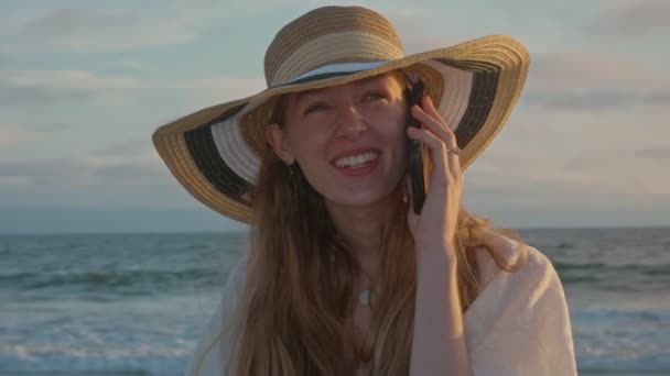 O tânără vorbind la telefon lângă ocean în timpul apusului de soare — Videoclip de stoc