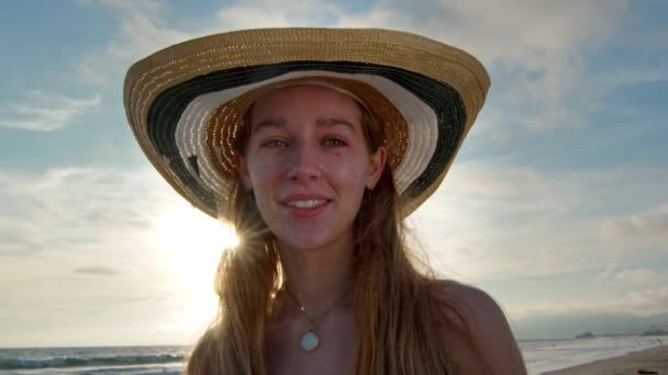 Jeune femme avec un grand chapeau à la plage souriant à la caméra — Video