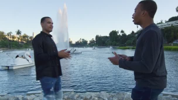 Dos jóvenes sosteniendo teléfonos mientras se hablan en el parque — Vídeos de Stock