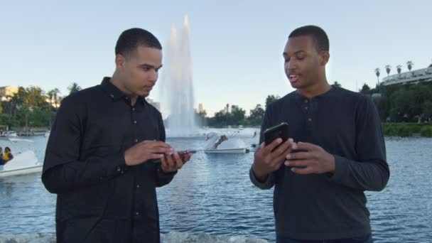 Dois jovens usando seus celulares em um parque — Vídeo de Stock