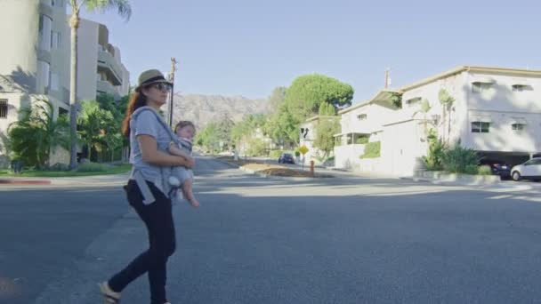 Femme portant son bébé sur un transporteur alors qu'elle traverse une rue — Video