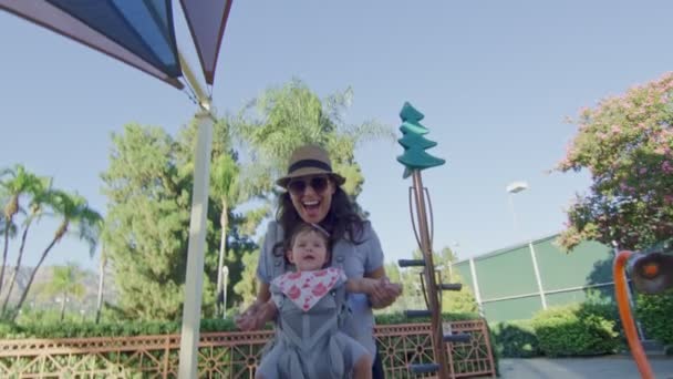 POV sliding on slide at playground to meet mother with baby on carrier — Stock Video