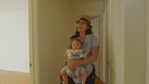 Glückliche Frau mit Baby im Tragetuch läuft durch eine leere Wohnung — Stockvideo