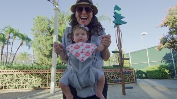 POV coming down on slide at park to meet mother with baby on carrier — ストック動画