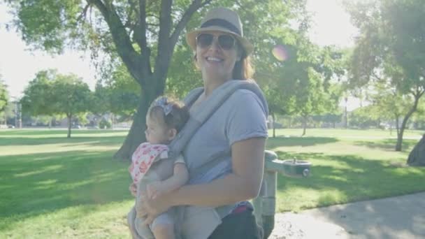 Счастливая женщина, идущая по парку с ребенком на носильщике — стоковое видео