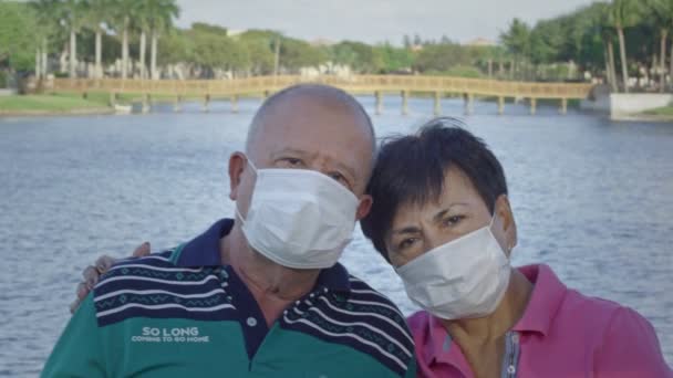 Elderly couple looking at camera while wearing face masks in front of a lake — Stock Video