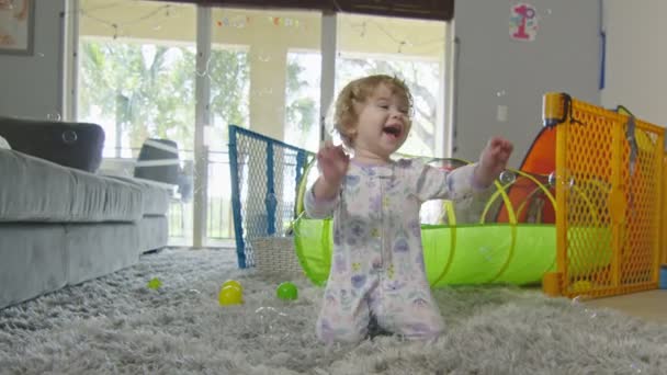 Slow motion van klein meisje lachen en spelen met bubbels thuis — Stockvideo