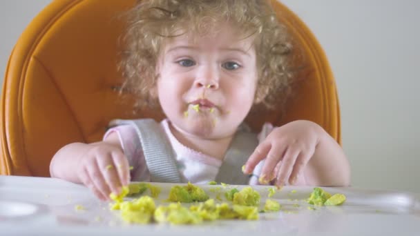 Baby dívka na vysoké židli s úsměvem a jíst avokáda s rukama — Stock video