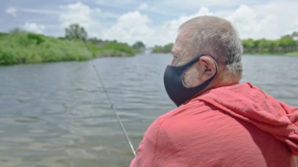 Uomo anziano indossando maschera protettiva durante la pesca su un lago — Video Stock