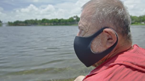 Detailní záběr staršího muže v masce obličeje před jezerem — Stock video