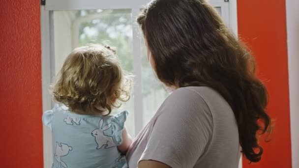 Madre usando mascarilla mientras saluda con su hija a través de la ventana — Vídeo de stock