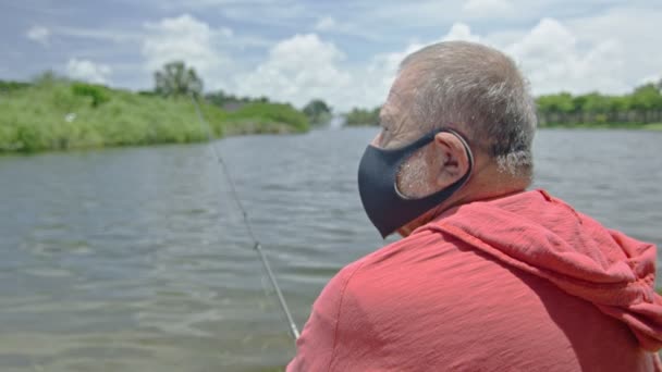 Homem sênior usando uma máscara facial enquanto pescava em um lago — Vídeo de Stock