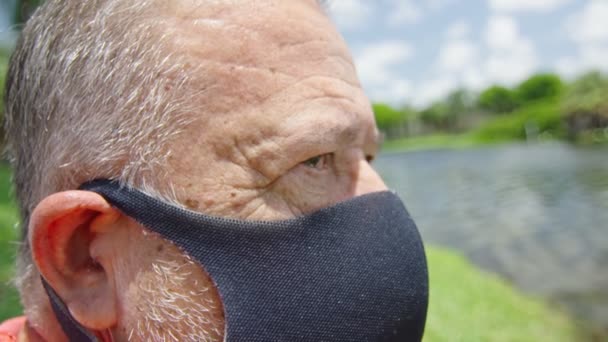 Elderly man with intense look wearing a protective face mask in front of a lake — Stock Video