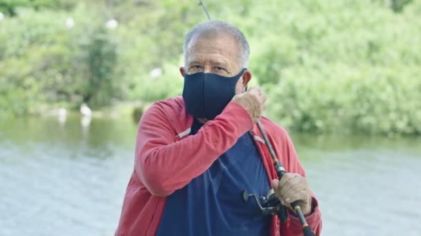 Gros plan d'un homme âgé au regard intense portant un masque protecteur devant un lac — Video