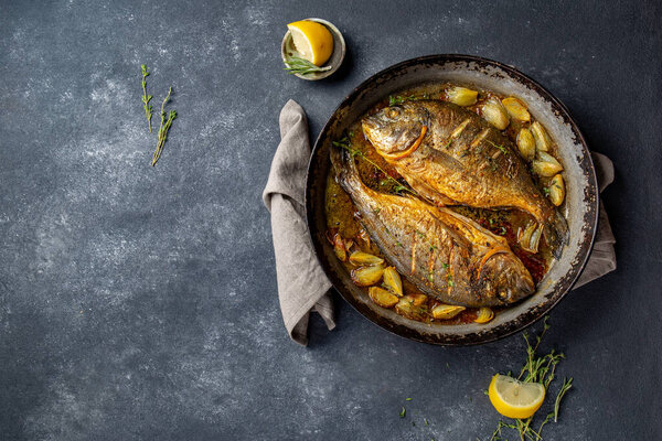 Baked sea bream or dorada with onion and herbs in pan on dark background