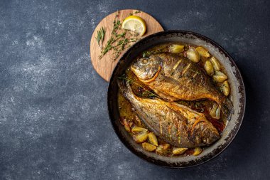 Koyu arkaplanda soğan ve otlarla pişirilmiş deniz mahsulü veya dorada.