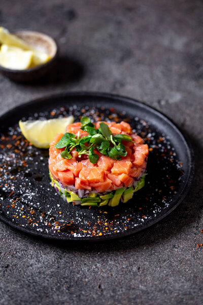 Raw salmon, avocado purple onion salad served in culinary ring on black plate. Black concrete background.
