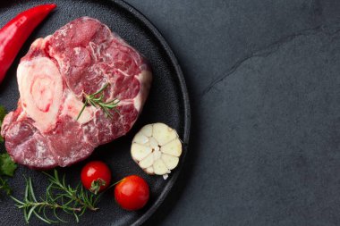 Çiğ ossobuco con şifalı otlar, sarımsak ve siyah tabakta biber. Koyu arkaplan