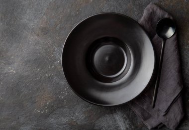 Gıda arka planı siyah boş tabak, gri peçete ve siyah kaşık arka planda.