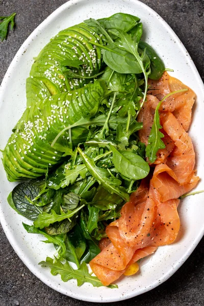 Salada com baixo teor de carboidratos. Espinafre, salada de rúcula com abacate e salmão. Fundo de concreto preto, placa branca, vista superior — Fotografia de Stock