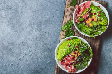 Düşük karbonhidrat kasesi. Taze salata, yeşil ıspanak, roka, avokado beyaz kasede jambon, gri arka plan, üst manzara..